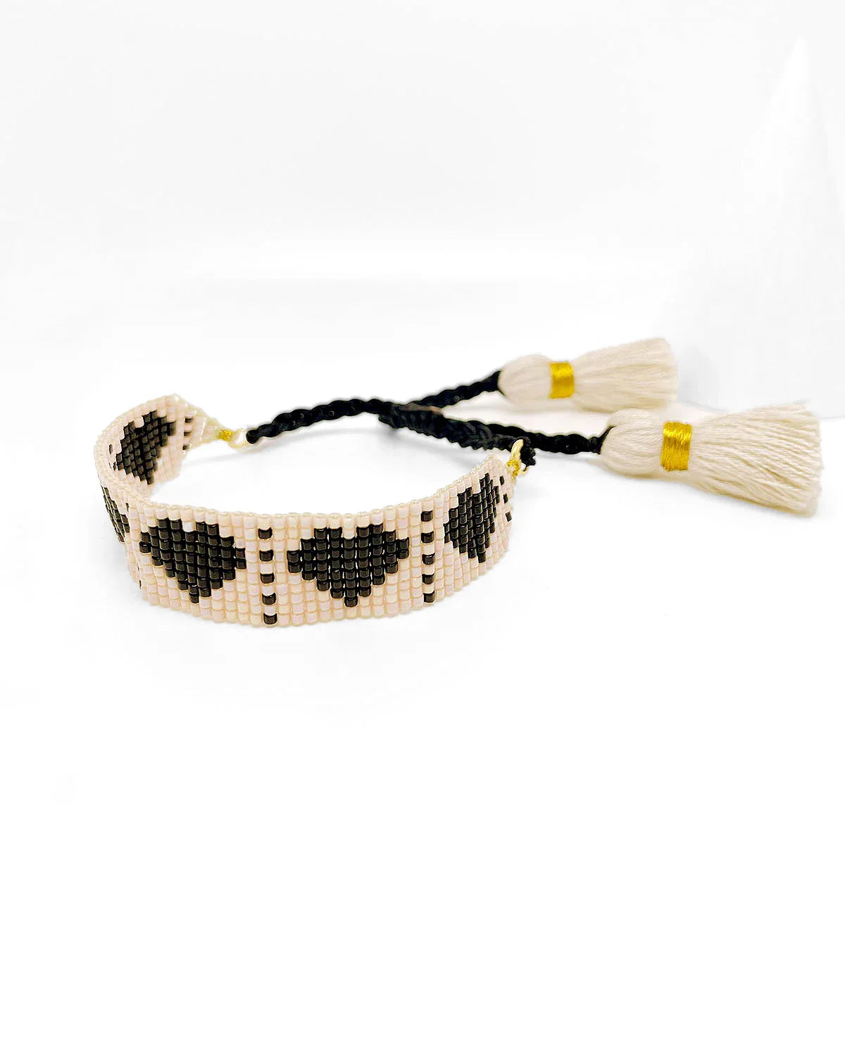 Pulsera Corner 2 Corner diseño exclusivo de Erika Valencia con corazones negros y detalle de borlas crema