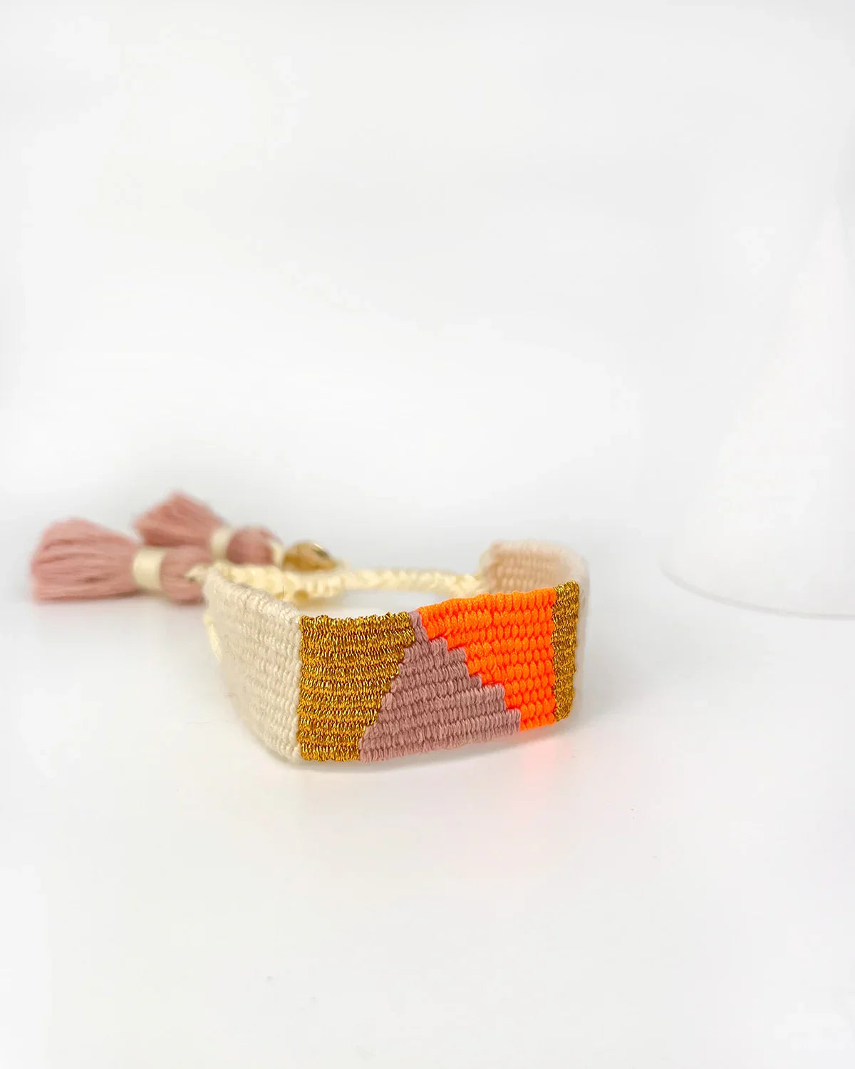 Handmade woven bracelet by Erika Valencia with orange pink and gold geometric pattern and tassels