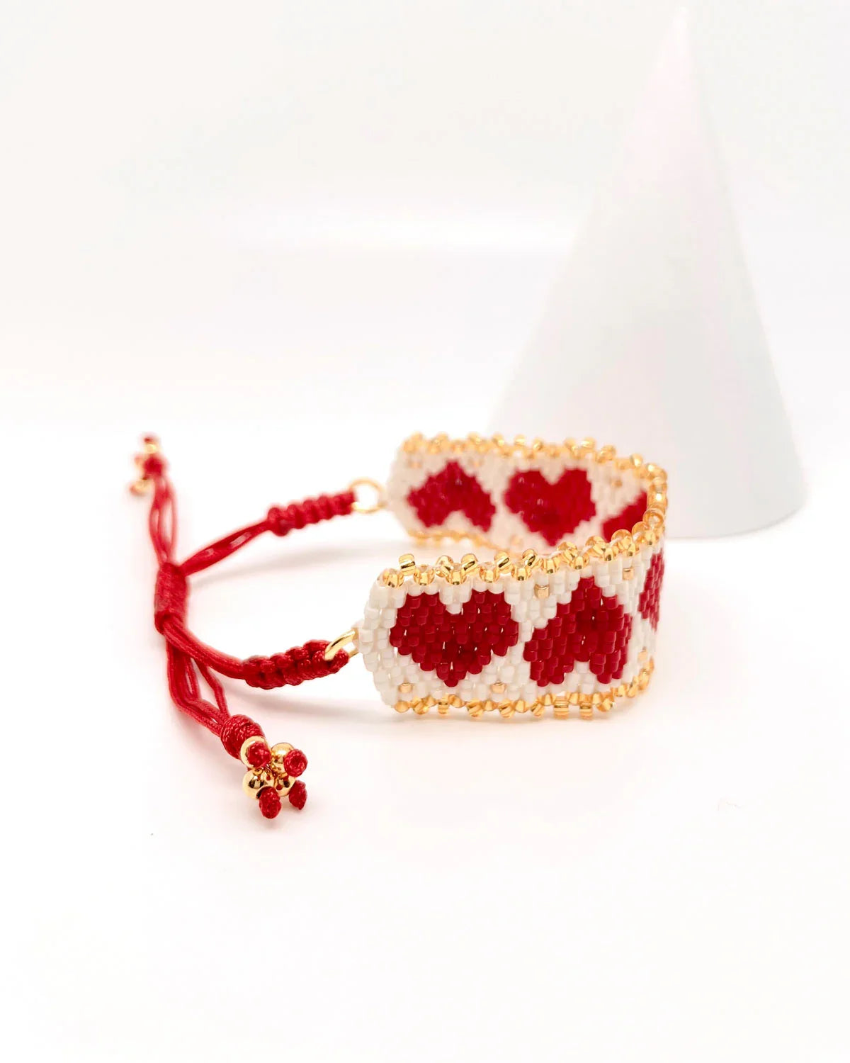 Pulsera artesanal de corazones rojos y blancos con detalles dorados y ajuste con cordón rojo